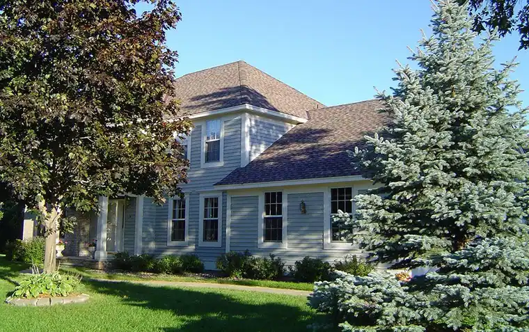 Two-storey blue house with a new dark shingle roof behind a blue spruce