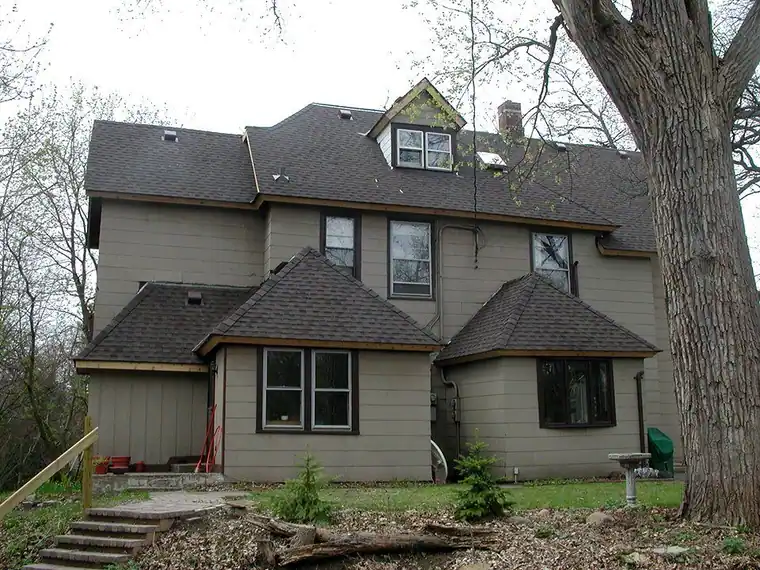 Tan foursquare house with hipped bays under dark shingle