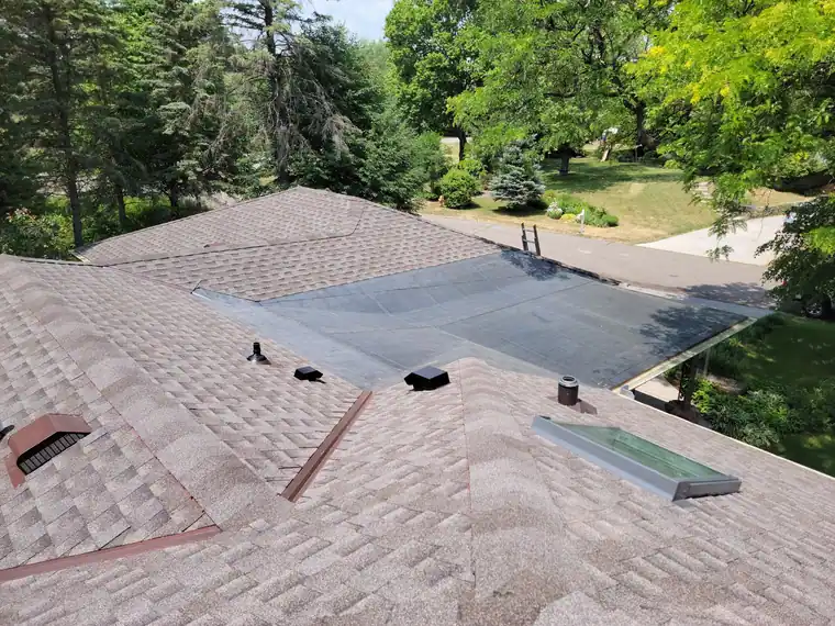 Roof-level view of a shingle roof with a low-slope membrane section, vents and a skylight